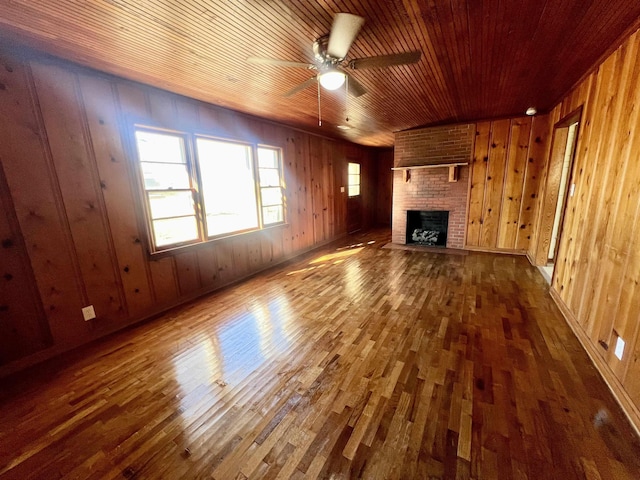 unfurnished living room with a fireplace, wood walls, ceiling fan, and wood ceiling