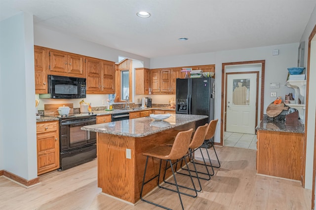 kitchen featuring sink, black appliances, a center island, and light stone counters