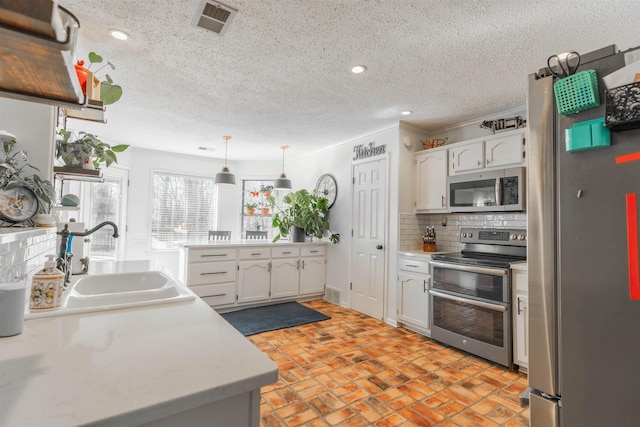 kitchen with pendant lighting, appliances with stainless steel finishes, sink, white cabinets, and decorative backsplash