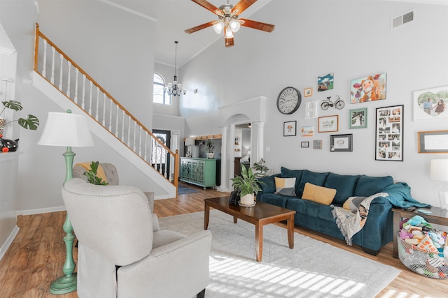 living room with high vaulted ceiling, hardwood / wood-style flooring, ornate columns, and ceiling fan with notable chandelier