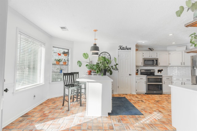 kitchen with crown molding, appliances with stainless steel finishes, decorative backsplash, white cabinets, and pendant lighting