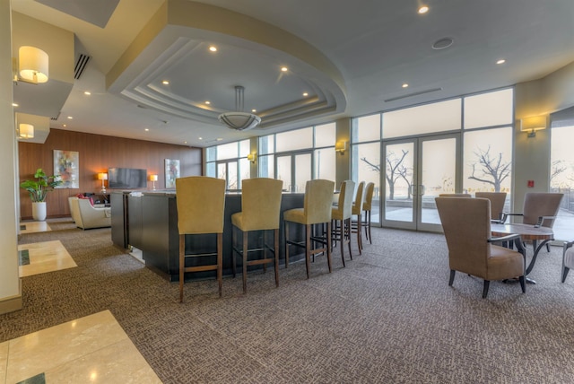 interior space with wooden walls, expansive windows, a tray ceiling, and french doors