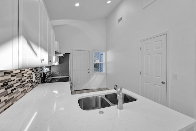 kitchen with white cabinets, decorative backsplash, sink, range with electric cooktop, and light stone counters