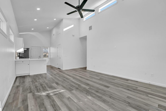 unfurnished living room featuring ceiling fan, a high ceiling, and light wood-type flooring