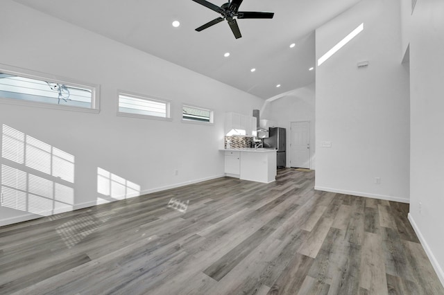 unfurnished living room featuring light wood-type flooring, ceiling fan, high vaulted ceiling, and plenty of natural light