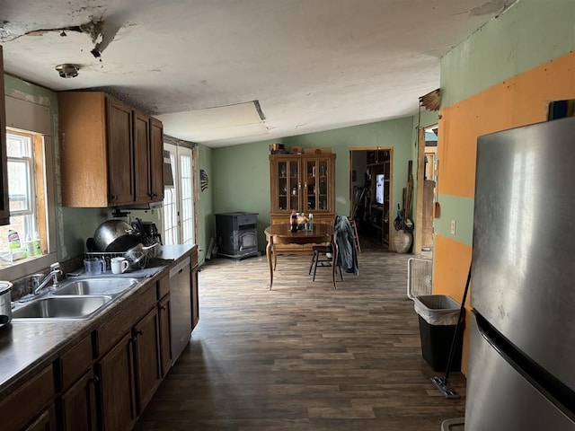 kitchen with lofted ceiling, sink, dark wood-type flooring, stainless steel appliances, and a wood stove