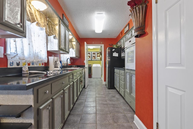 kitchen featuring black appliances, washing machine and dryer, a textured ceiling, and sink