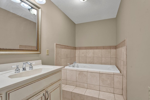 bathroom featuring a textured ceiling, a relaxing tiled tub, and vanity