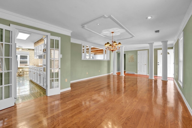 spare room with light hardwood / wood-style floors, ornamental molding, ornate columns, and a chandelier