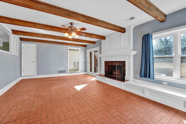 unfurnished living room with ceiling fan, beamed ceiling, and a fireplace