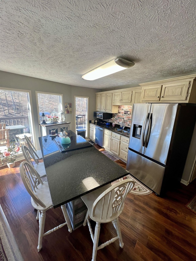 kitchen featuring dark hardwood / wood-style flooring, appliances with stainless steel finishes, cream cabinetry, a kitchen bar, and decorative backsplash