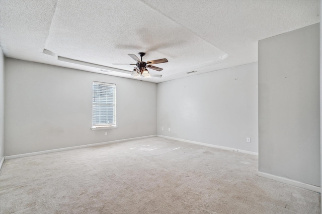 unfurnished room featuring ceiling fan, light colored carpet, a textured ceiling, and a tray ceiling