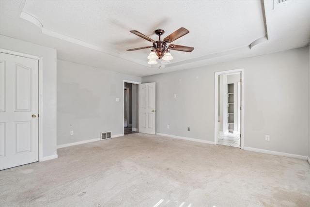 spare room with light carpet, a textured ceiling, a tray ceiling, and ceiling fan