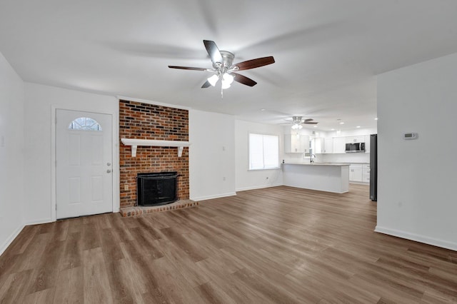 unfurnished living room featuring light wood finished floors, ceiling fan, a brick fireplace, and baseboards