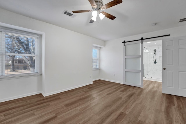 unfurnished bedroom with baseboards, a barn door, visible vents, and wood finished floors