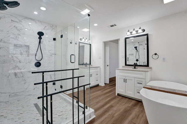 full bath featuring a marble finish shower, two vanities, visible vents, wood finished floors, and a freestanding tub