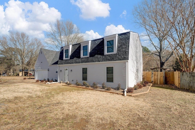 colonial inspired home with an attached garage, a shingled roof, fence, a gambrel roof, and a front yard