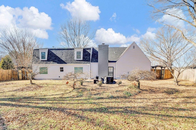 back of property with a shingled roof, a chimney, and fence