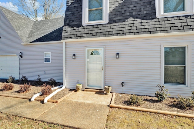 view of exterior entry featuring roof with shingles, an attached garage, and mansard roof