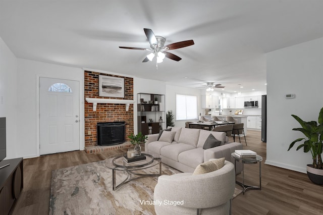 living area featuring a ceiling fan, a brick fireplace, baseboards, and wood finished floors