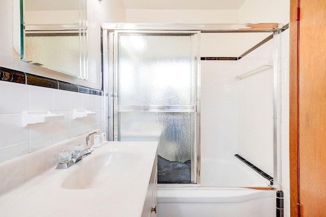 bathroom featuring vanity, backsplash, bath / shower combo with glass door, and tile walls