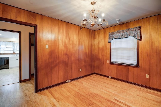 spare room featuring wood walls, a chandelier, and light wood-type flooring