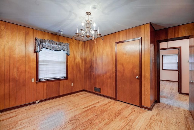 empty room with wood walls, a chandelier, and light wood-type flooring