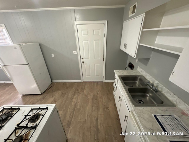 kitchen featuring white appliances, hardwood / wood-style floors, white cabinets, sink, and wood walls