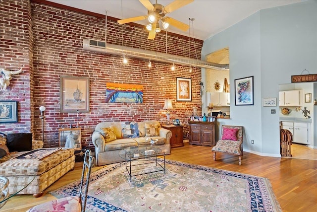 living room featuring a high ceiling, ceiling fan, brick wall, and light hardwood / wood-style flooring