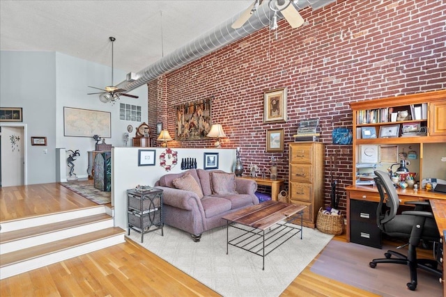 living room featuring light wood-type flooring, a towering ceiling, brick wall, and ceiling fan