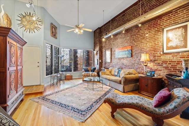 living room with light wood-type flooring, ceiling fan, brick wall, and a high ceiling