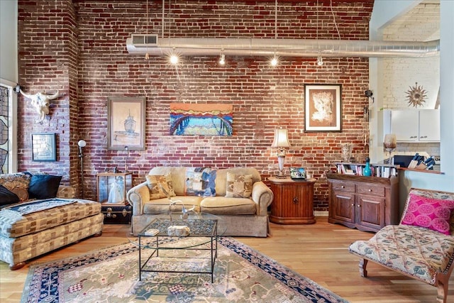 living room with a high ceiling, brick wall, rail lighting, and light wood-type flooring