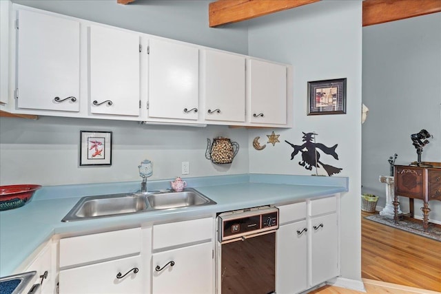 kitchen with black dishwasher, white cabinetry, sink, light wood-type flooring, and beam ceiling