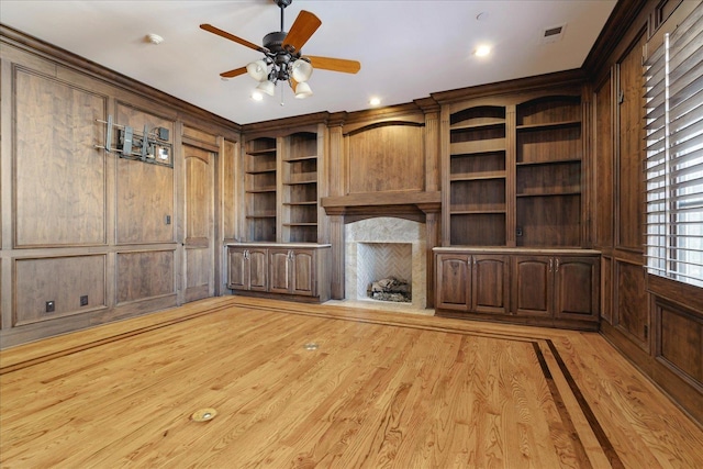 unfurnished living room with ceiling fan, wooden walls, and light hardwood / wood-style floors