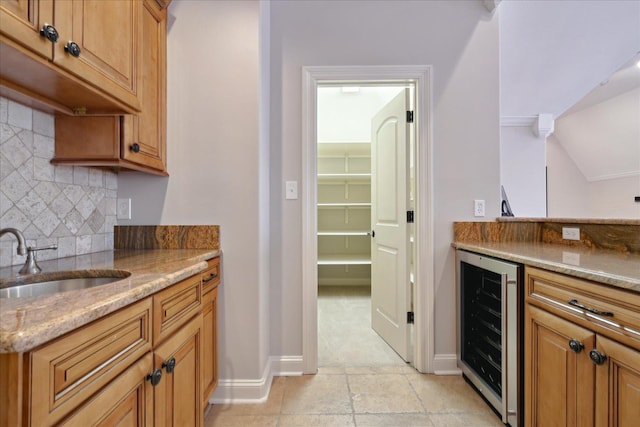 kitchen with light stone counters, sink, decorative backsplash, and wine cooler