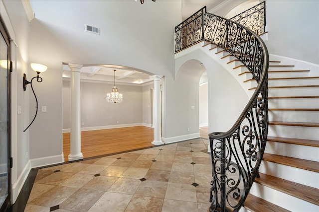 foyer entrance with a towering ceiling, coffered ceiling, ornate columns, and crown molding