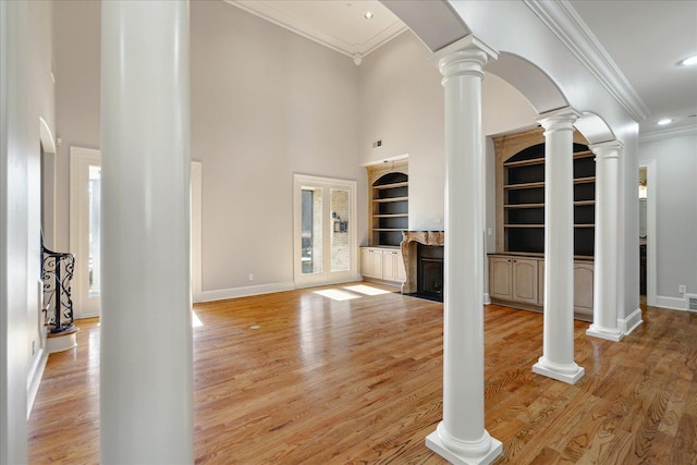 unfurnished living room with decorative columns, built in shelves, light hardwood / wood-style flooring, and ornamental molding