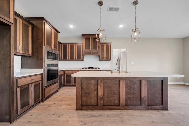 kitchen with light hardwood / wood-style floors, sink, decorative light fixtures, an island with sink, and stainless steel appliances