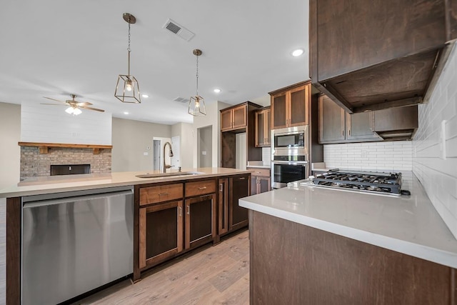 kitchen featuring appliances with stainless steel finishes, premium range hood, light hardwood / wood-style flooring, pendant lighting, and backsplash