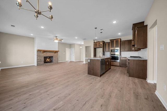 kitchen featuring ceiling fan, appliances with stainless steel finishes, decorative light fixtures, light hardwood / wood-style flooring, and an island with sink