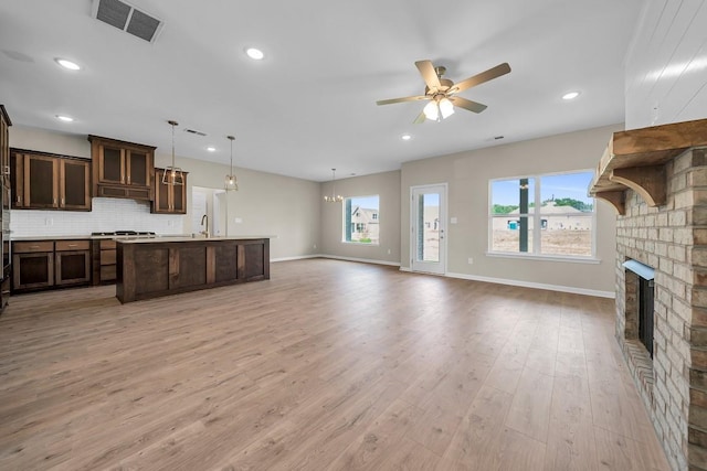 unfurnished living room with a brick fireplace, light hardwood / wood-style floors, sink, and ceiling fan