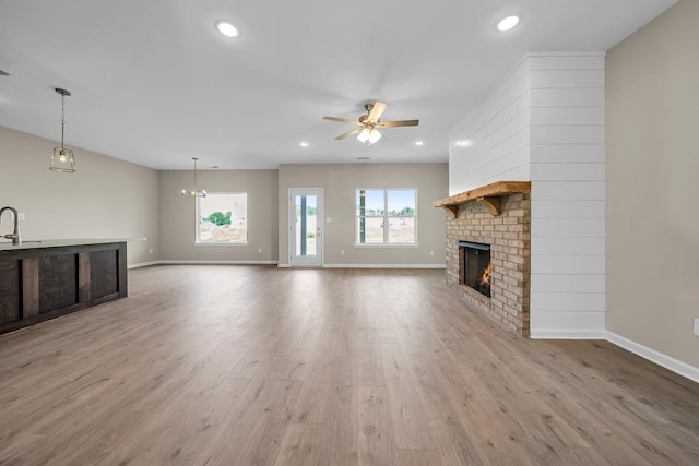 unfurnished living room with light wood-type flooring, ceiling fan, a fireplace, and sink