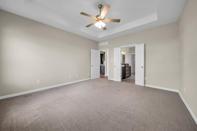 unfurnished bedroom with ceiling fan, carpet, and a tray ceiling