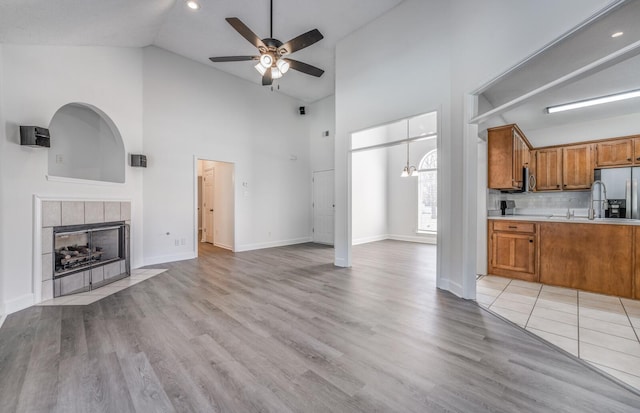 unfurnished living room with high vaulted ceiling, ceiling fan with notable chandelier, light hardwood / wood-style flooring, and a fireplace