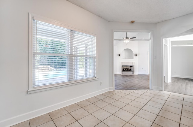 tiled empty room with ceiling fan, a textured ceiling, and a tiled fireplace