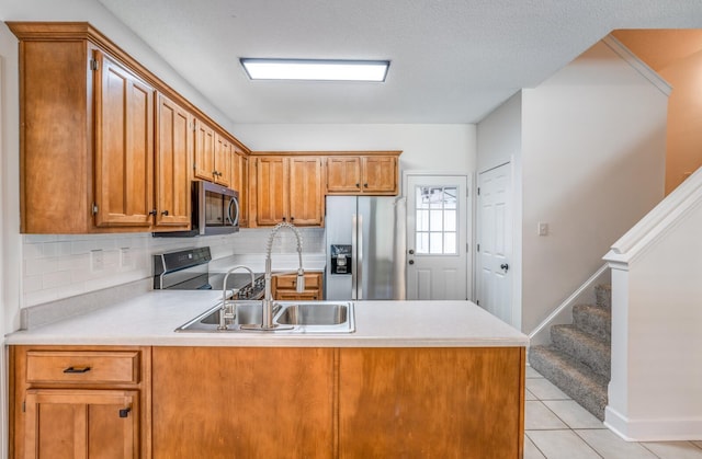 kitchen featuring appliances with stainless steel finishes, sink, kitchen peninsula, backsplash, and light tile patterned flooring