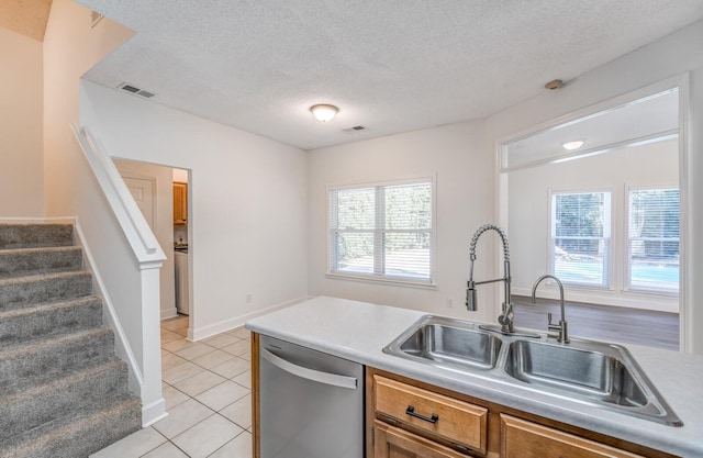 kitchen with sink, a textured ceiling, light tile patterned floors, and stainless steel dishwasher