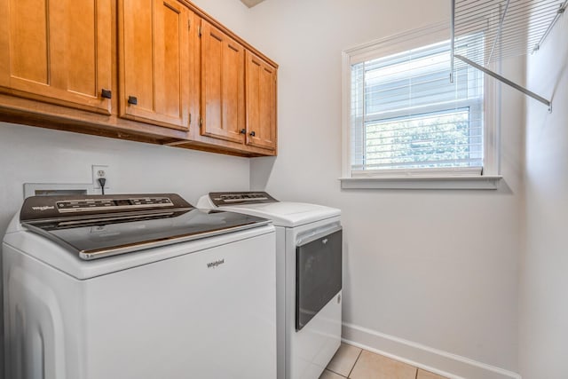 clothes washing area featuring washer and clothes dryer, cabinets, and light tile patterned flooring