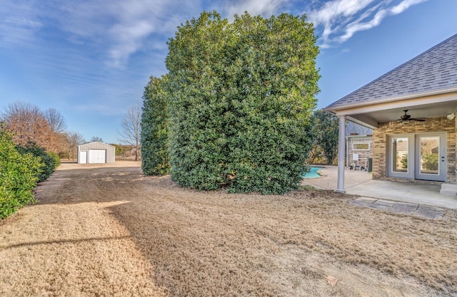 view of yard with ceiling fan, a patio area, an outbuilding, and a garage