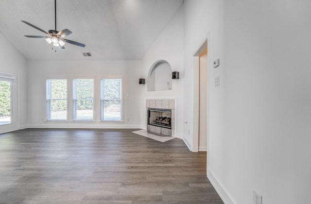 unfurnished living room with ceiling fan, dark wood-type flooring, high vaulted ceiling, and a tiled fireplace